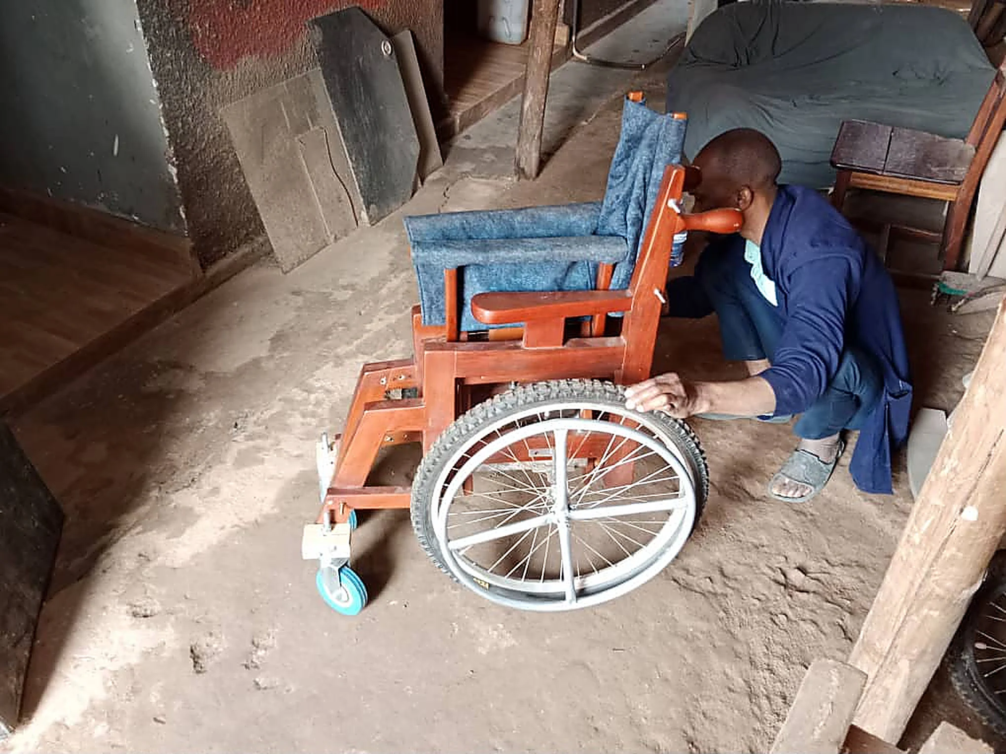 A craftsman adjusting the wheel of a wooden wheelchair in the workshop.